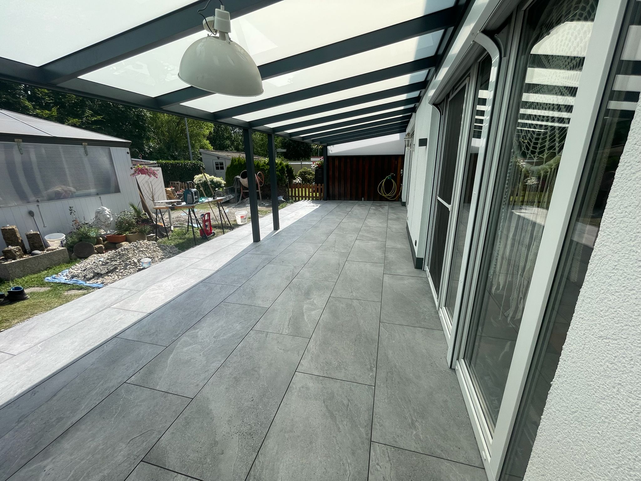 Überdachte Terrasse mit großformatigen Feinsteinzeug-Platten – eigene Pflasterarbeit von TOJA Bau